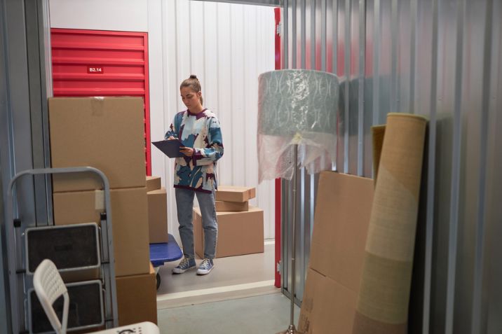 Young woman checking list on clipboard when putting belongings in rented self-storage