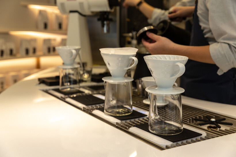 Three pour-over coffee drippers on glass servers at a café counter. - hospitality outsourcing