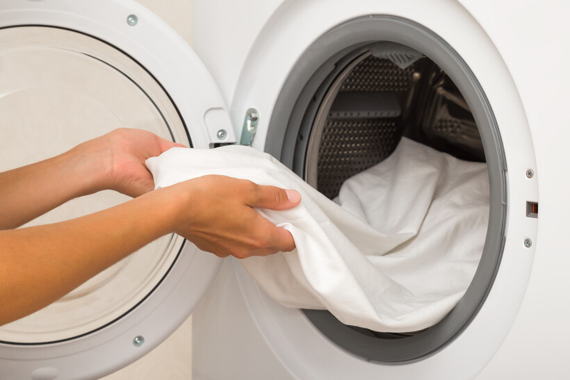 Close-up of hands unloading a white sheet from an open washing machine. - hospitality outsourcing