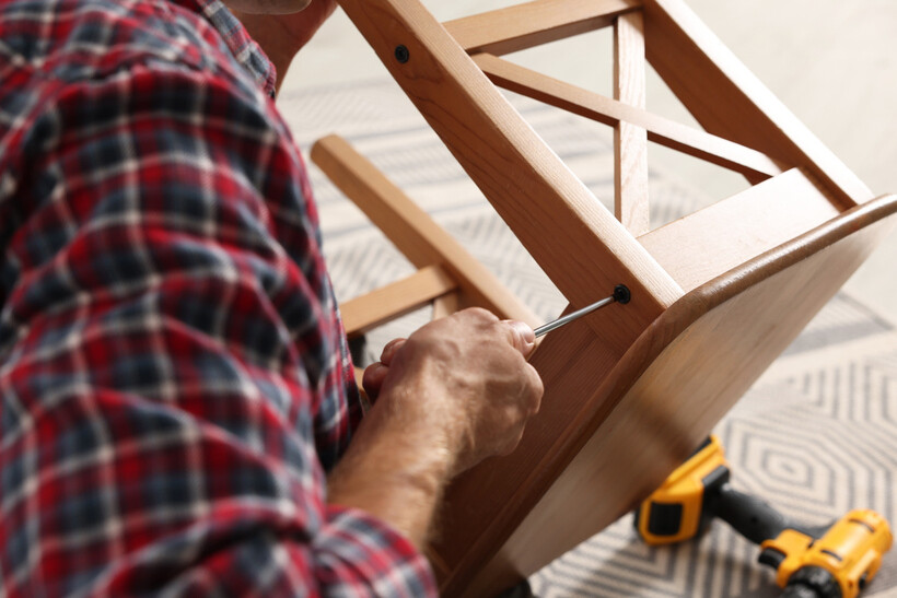 A man in a plaid shirt screwing together the frame of a wooden stool. - café tasks