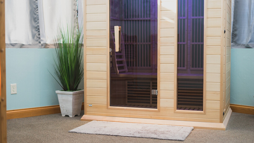 A pale timber infrared sauna cabin with a glass door and purple interior lighting. - infrared vs traditional sauna