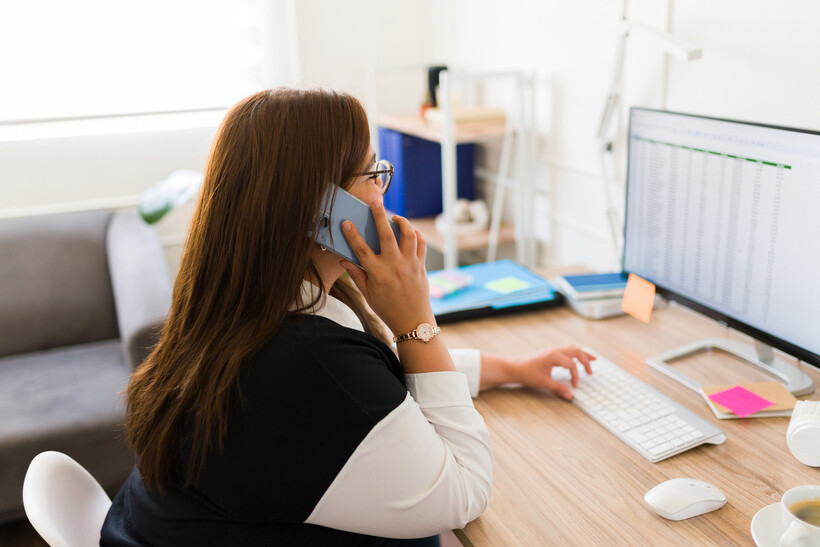 A woman balances a phone call and keyboard work at a sunlit home office desk. - landscaping tasks