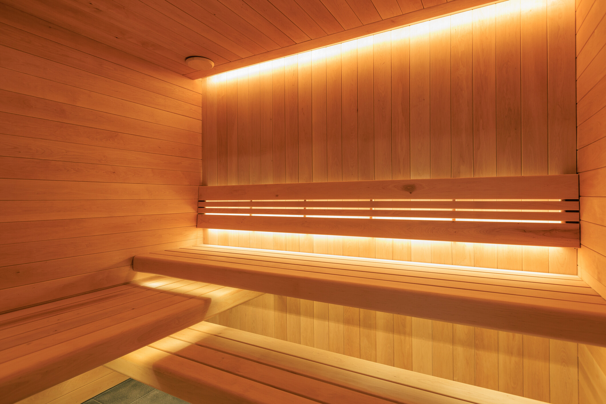Clean wooden interior of a home sauna featuring tiered slatted benches and warm indirect LED strip lighting. - how much does it cost to build a home sauna
