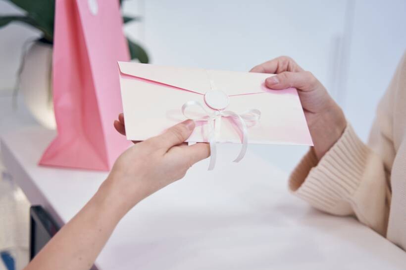 baby shower gift ideas - Pink ribbon-tied envelope exchanged beside a matching gift bag