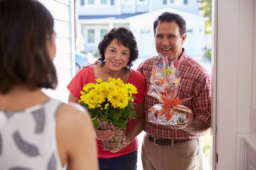 housewarming gift ideas - Older couple arriving with yellow flowers and a wrapped gift at a front door