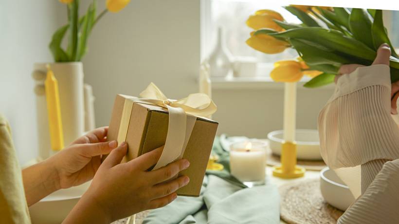 housewarming gift ideas - Wrapped gift box with ribbon beside yellow tulips and candles