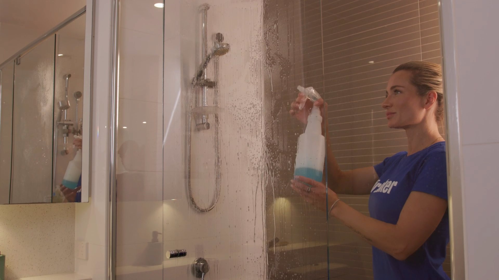 a cleaner using cleaning solution mix to spray and clean to clean a shower glass