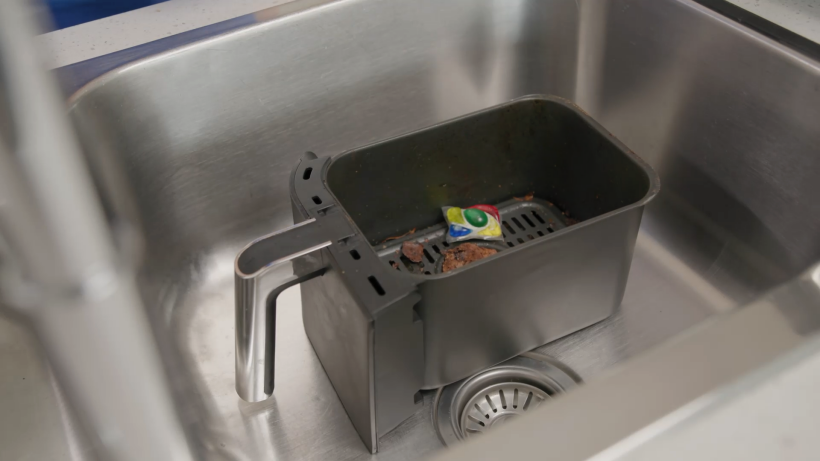 a dirty air fryer tray with a dishwashing tablet in the sink - how to clean air fryer