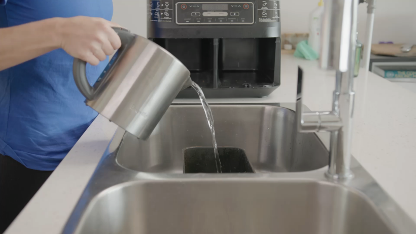 a cleaner holding a kettle with hot water and pouring it into the air fryer basket - cleaning air fryer