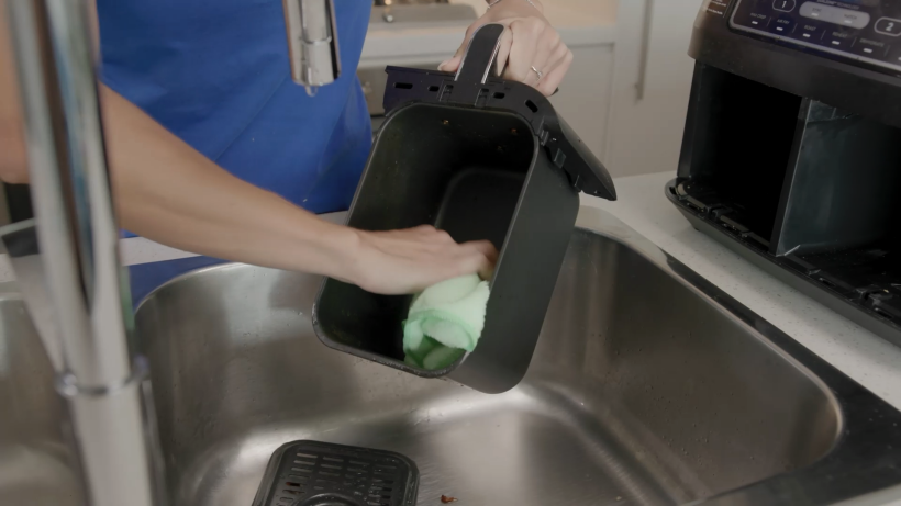 a cleaner just finished cleaning the air fryer basket and using a microfibre towel to wipe it clean - how to clean air fryer