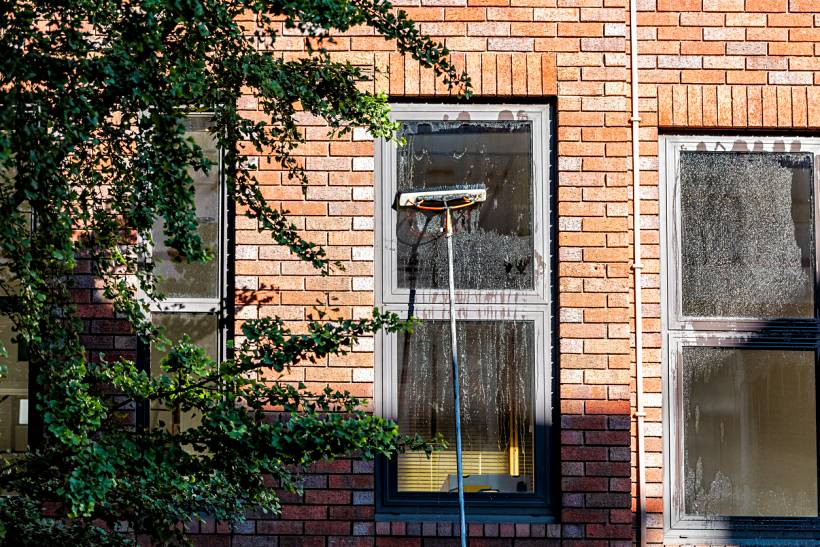 how much does window cleaning cost - Exterior window cleaning on a brick building with a long-handled squeegee
