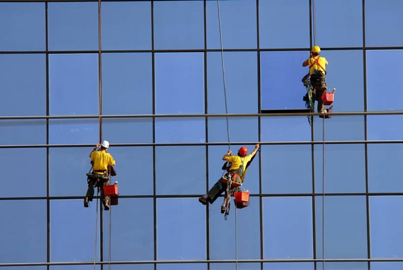 how much does window cleaning cost - Three rope access window cleaners working on a high-rise glass facade