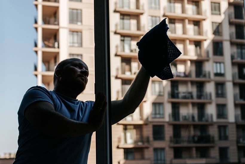how much does window cleaning cost - Man wiping an interior window with a cleaning cloth