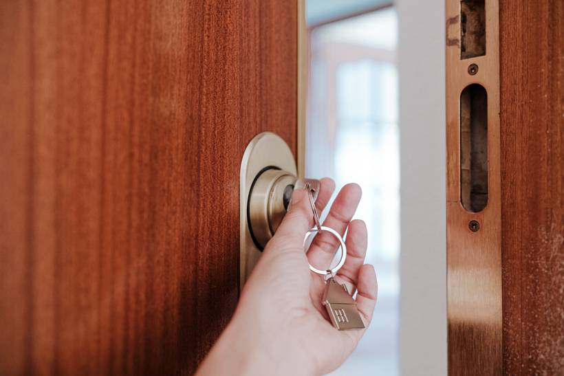 how much does house sitting cost - Hand unlocking a wooden front door with house keys