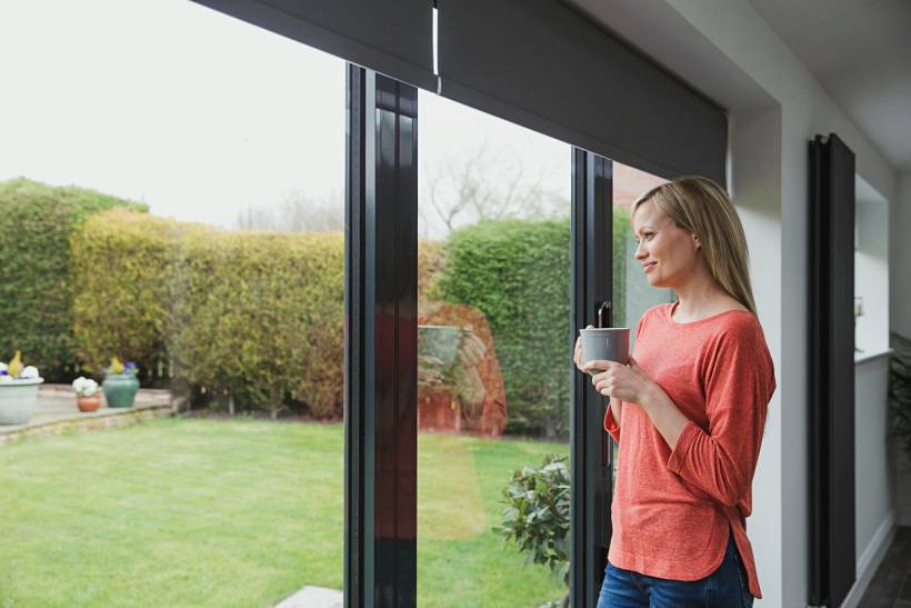 how much does house sitting cost - Woman holding a mug while looking out at a garden
