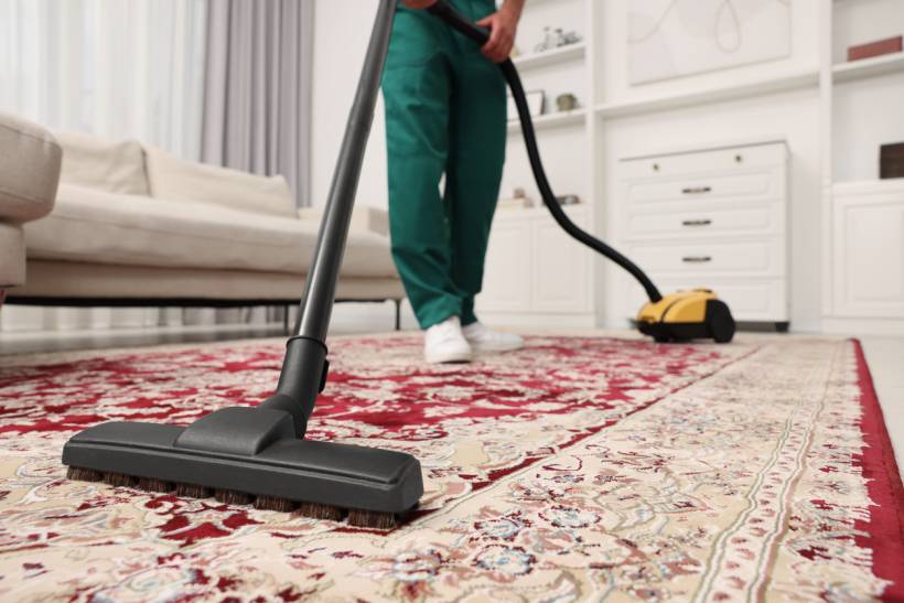 rug cleaning cost - Professional vacuuming patterned red rug in modern living room