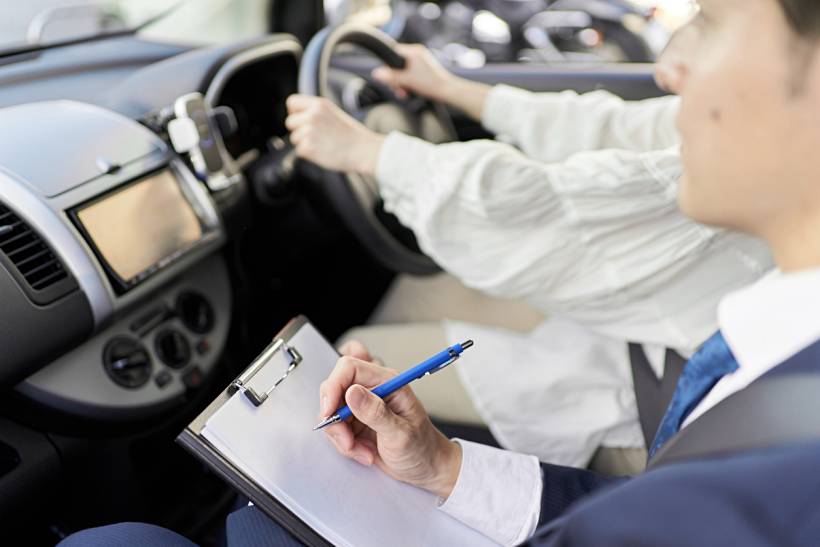 how much do driving lessons cost - Learner driver steering a car as an instructor records observations