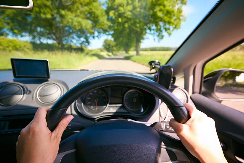 how much do driving lessons cost - Driver holding the steering wheel on a quiet rural road