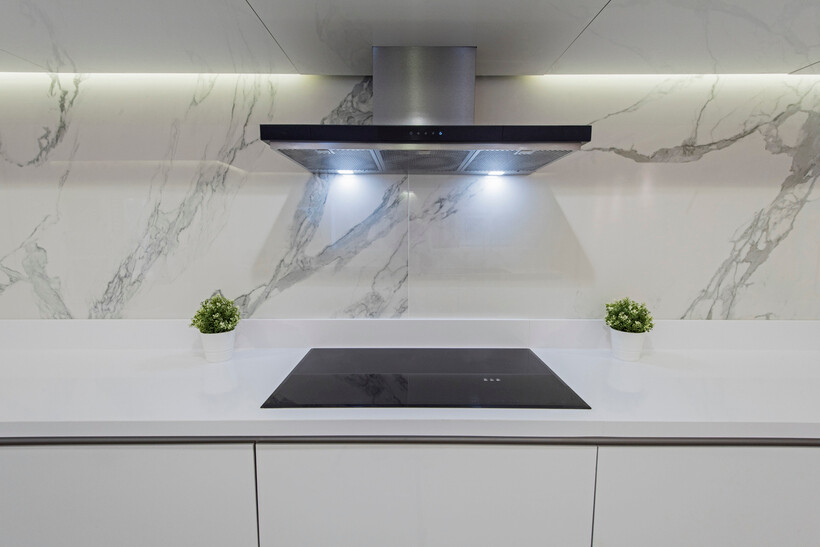 Large white marble-look porcelain tiles with grey veining behind a black induction cooktop. - kitchen splashback ideas