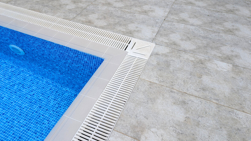 Grey stone-effect pool tiles meeting a drainage grate at the water line. - can you tile over pebblecrete