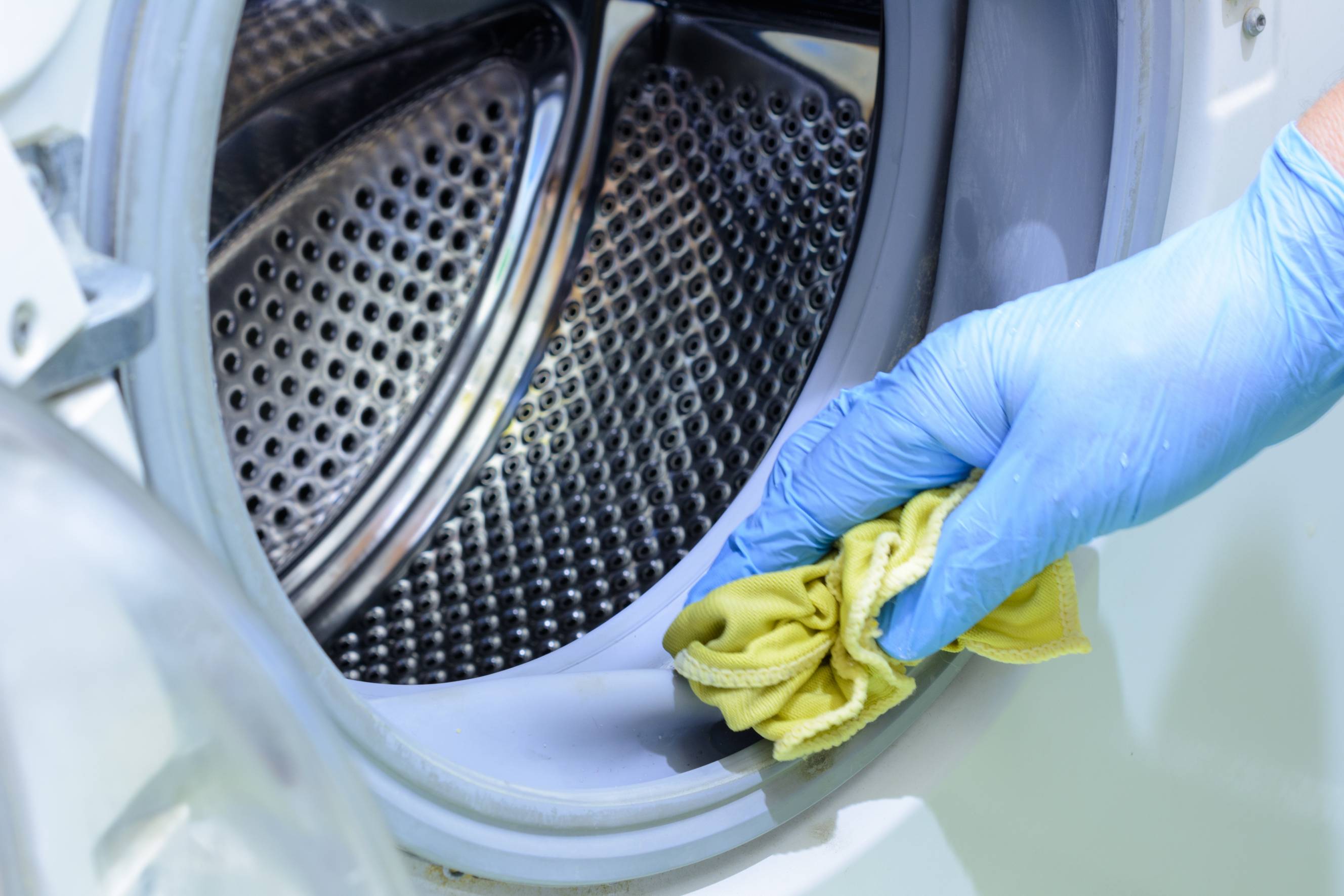 A Tasker performing washing machine cleaning with a wiping cloth and gloves