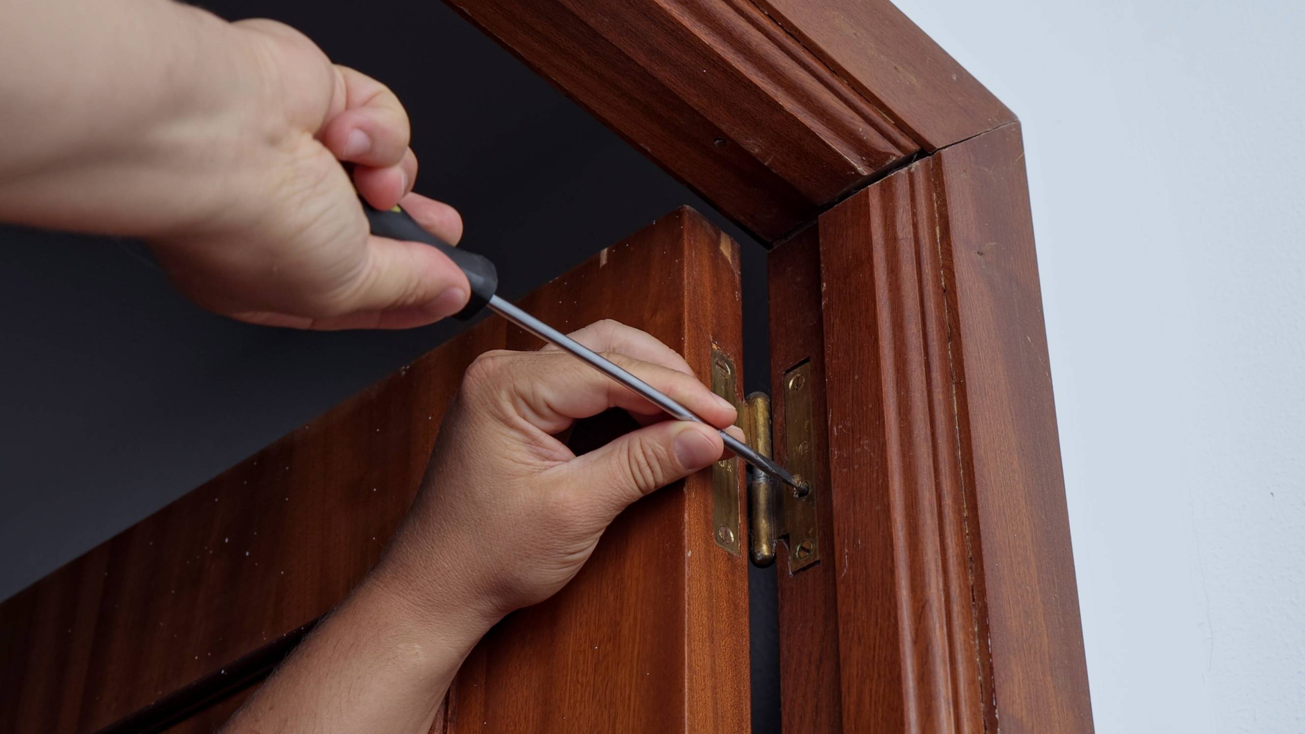 A handyman doing hinges repair using a screw driver on a wooden door