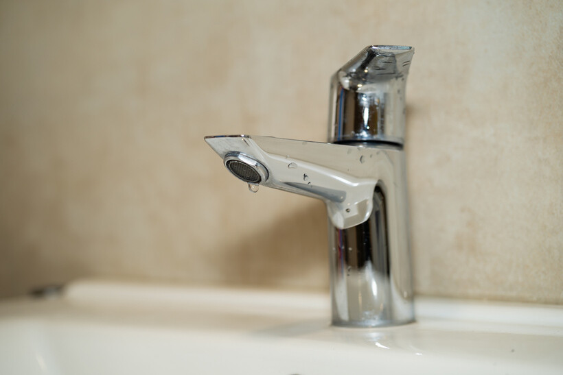 A chrome bathroom tap with an aerator nozzle and a water droplet at the spout. - low-flow taps and toilets