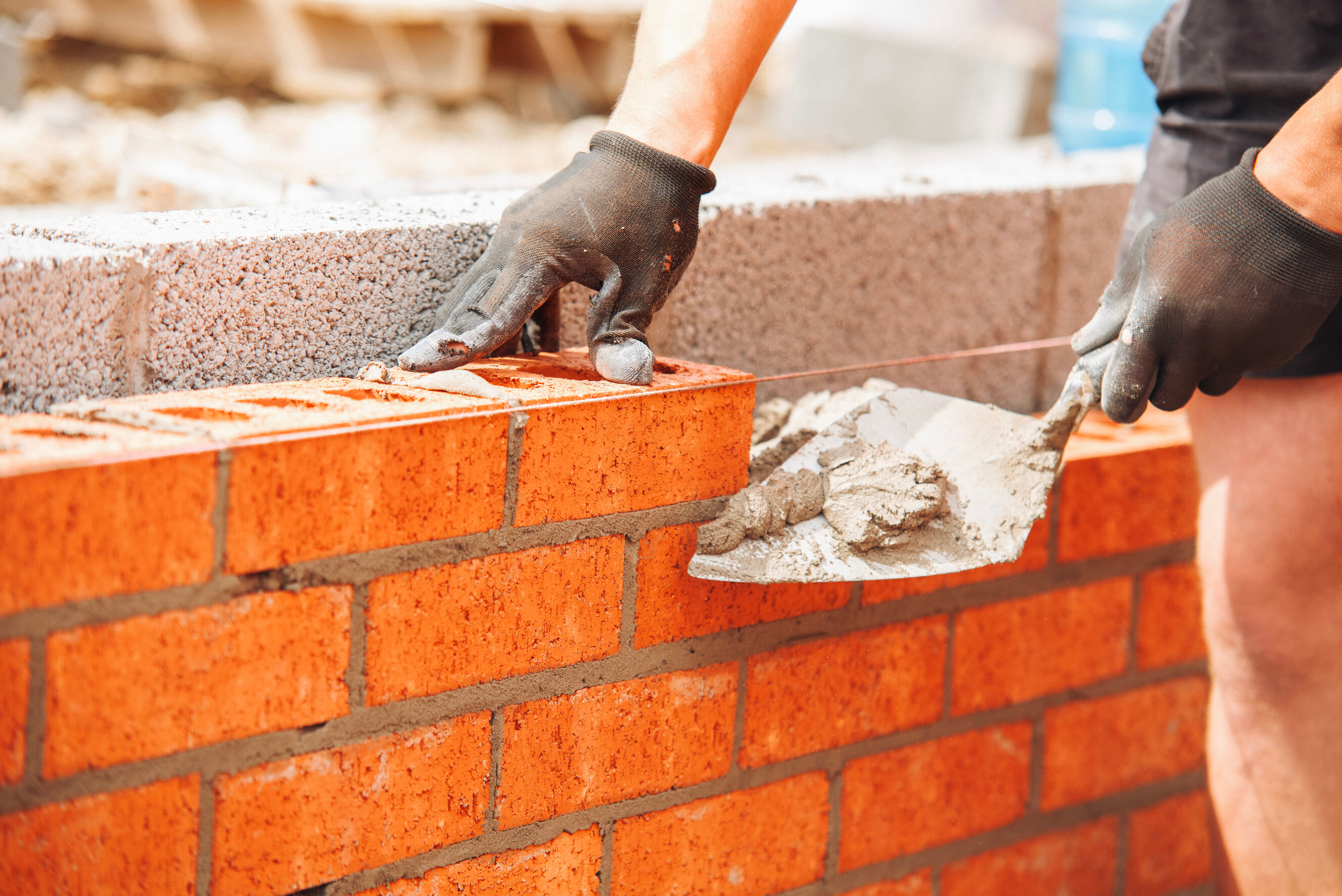 A bricklayer spreads mortar with a trowel while building a brick wall.