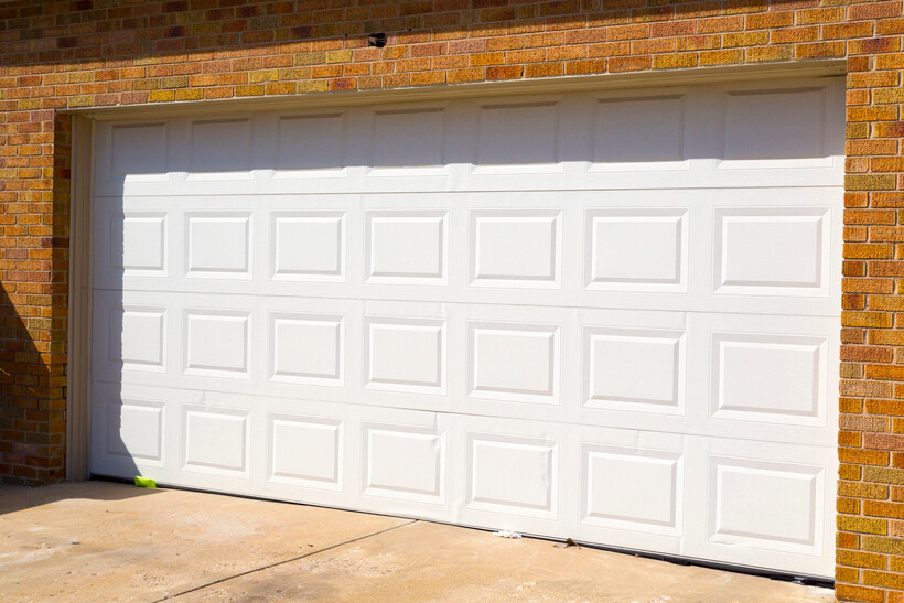 A white sectional garage door set into a red brick house exterior. - brick garage cost
