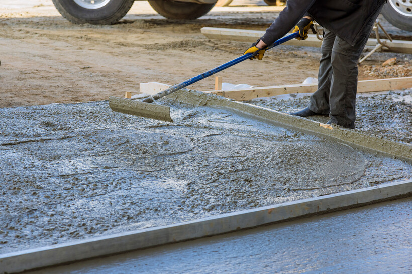 A worker smooths a freshly poured concrete slab with a long-handled float. - brick garage cost