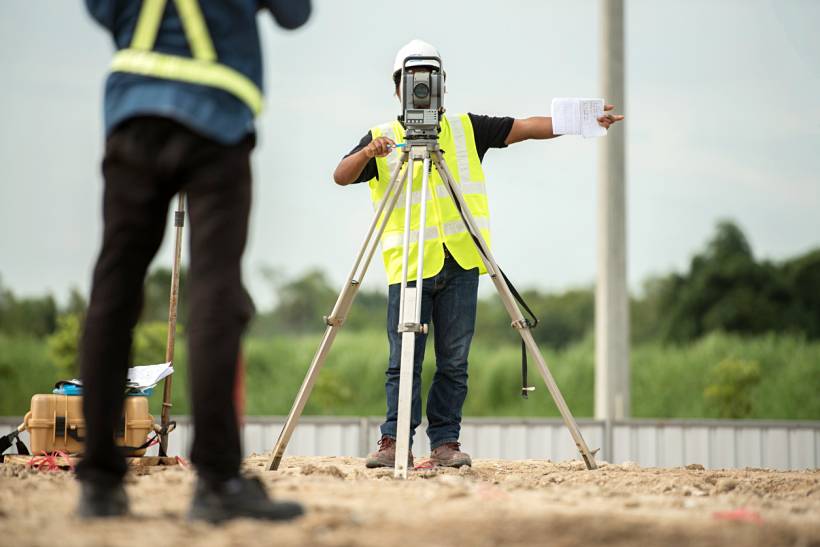 land survey cost - Land surveyor using surveying equipment with colleague