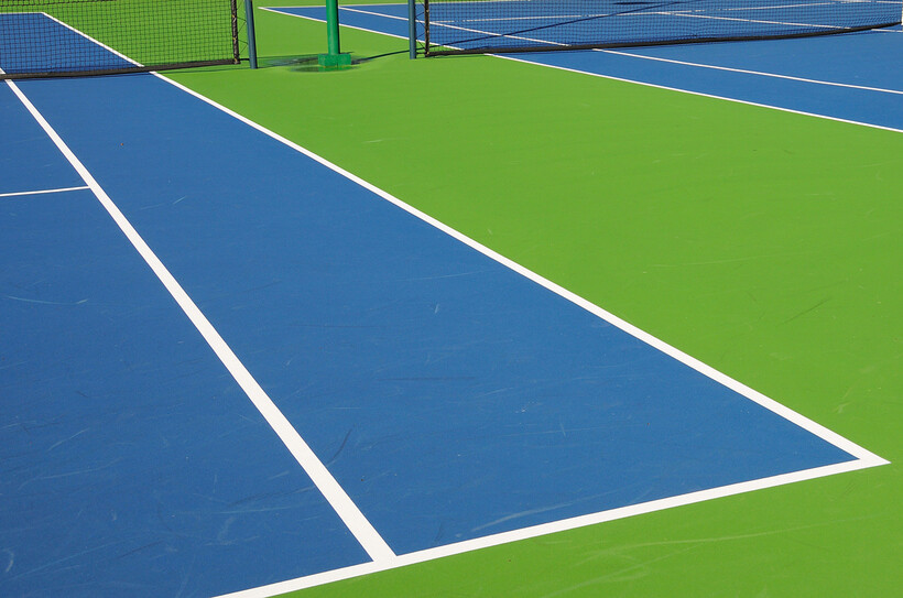 Two adjacent hard tennis courts with blue and green acrylic surfaces and white line markings. - tennis court resurfacing cost