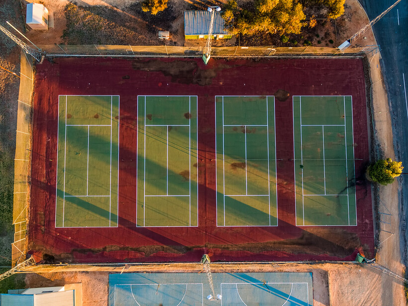 Aerial view of four tennis courts with worn red and green acrylic surfaces showing staining and uneven wear. - tennis court resurfacing cost