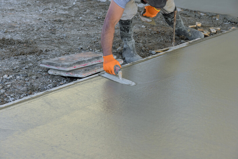 A tradesperson trowelling the surface of a freshly poured concrete base during a construction job. - tennis court resurfacing cost