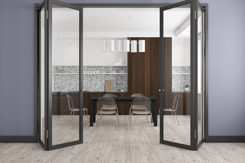 Dark-framed bifold doors open onto a modern kitchen and dining space. - bifold door installation cost