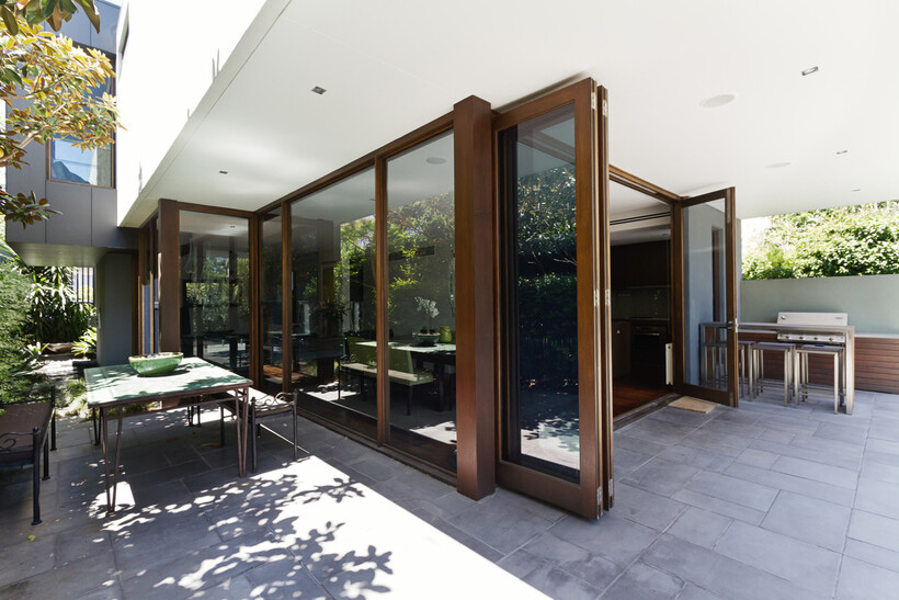 Wood-framed bifold doors stand open beside an outdoor barbecue area. - bifold door installation cost