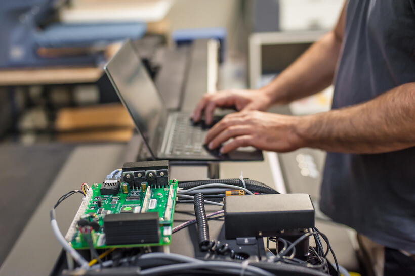 A technician typing on a laptop beside a disassembled circuit board. - computer repair cost