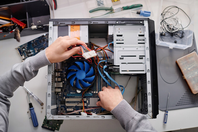 Hands connecting internal cables inside an open desktop computer case. - computer repair cost