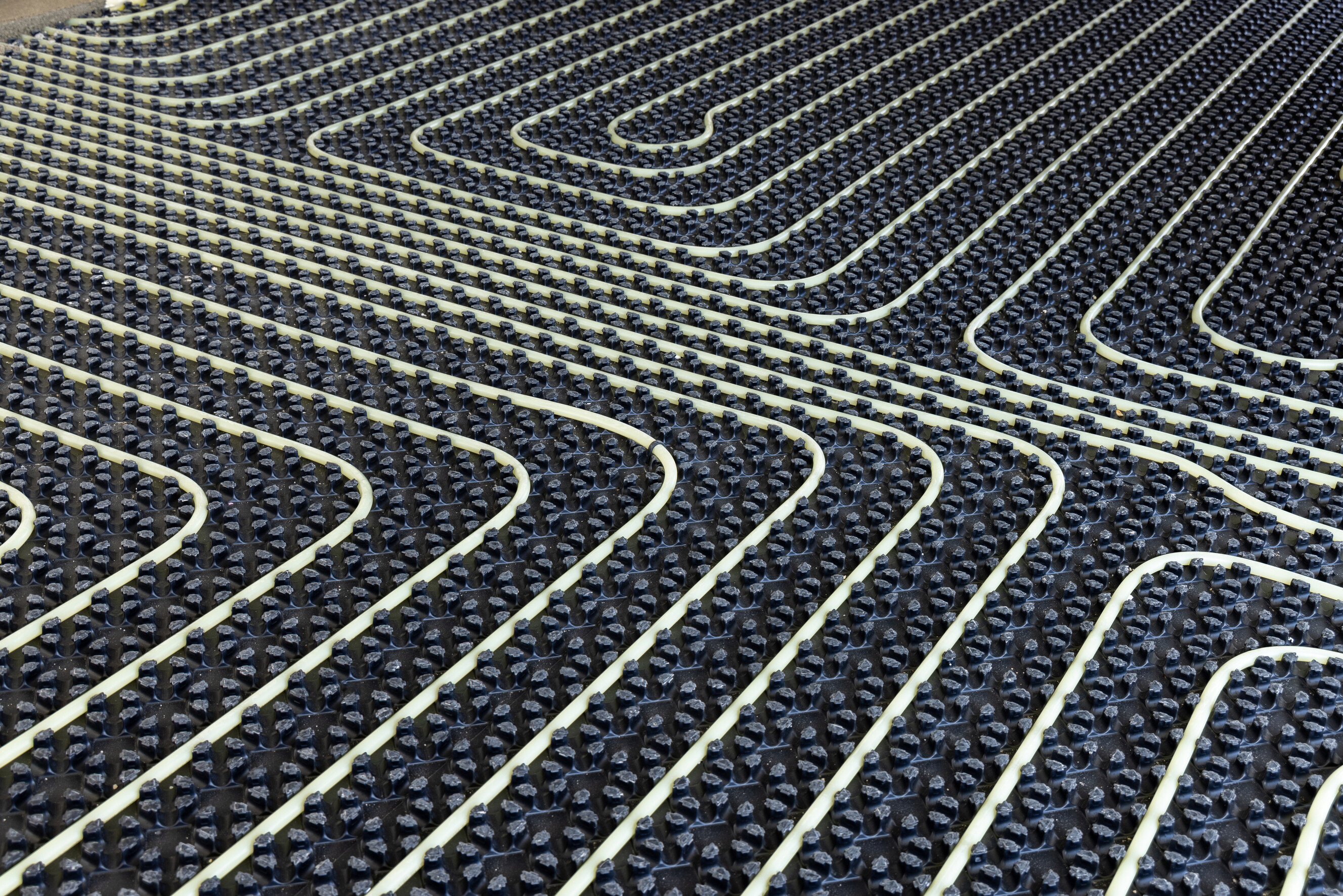 Rows of pale hydronic piping curve across dimpled insulation panels before the slab is poured.