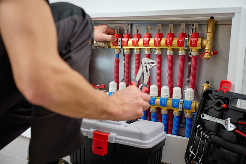A person adjusting a numbered manifold connecting red and blue hydronic pipe loops. - underfloor heating installation cost