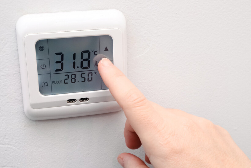 A finger adjusting a digital thermostat showing room and floor temperature readings. - underfloor heating installation cost
