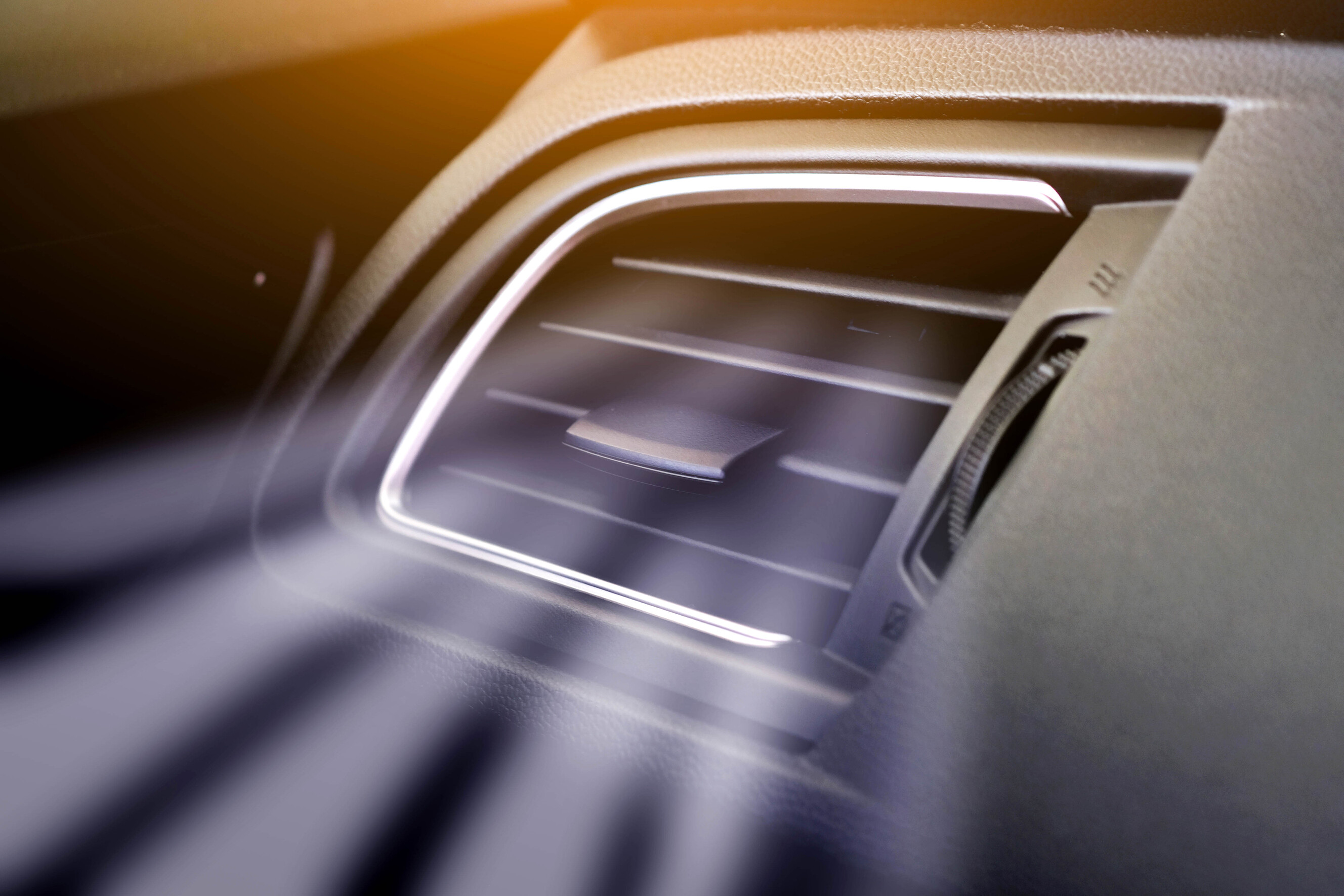Close-up of a car's dashboard air vent with chrome trim and vane detail.