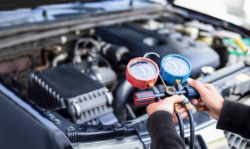 A technician holds a manifold gauge set while checking a car's air conditioning pressure. - car aircon regas cost