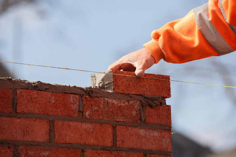 Close-up of a hi-vis worker positioning a brick during fence construction. - brick fencing cost