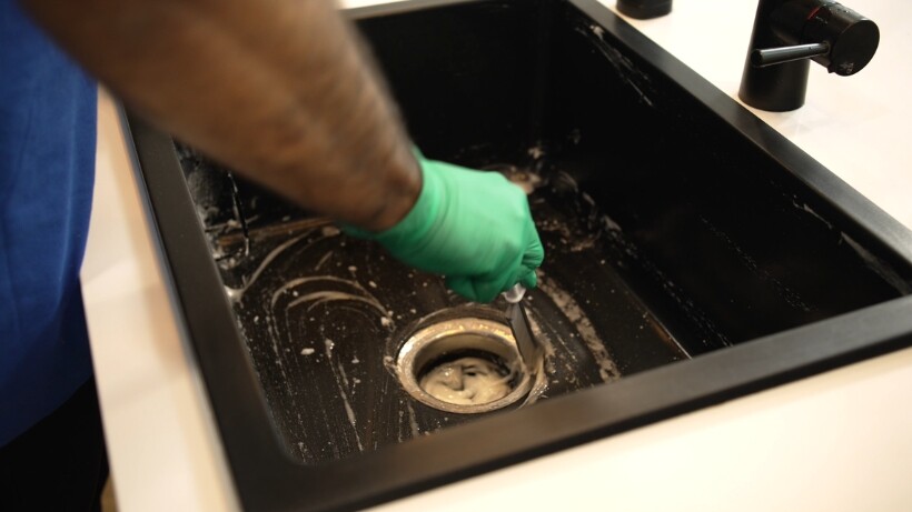 A professional cleaning the kitchen sink to remove grime and restore its shine.