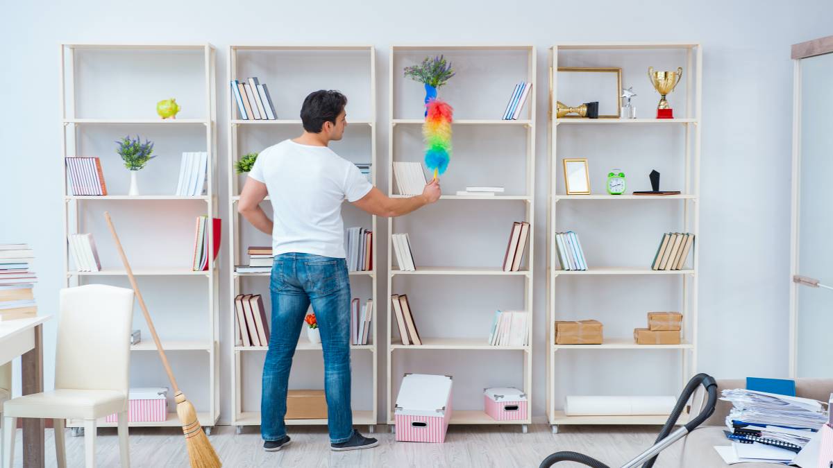 A man dusting bookshelves in an apartment
