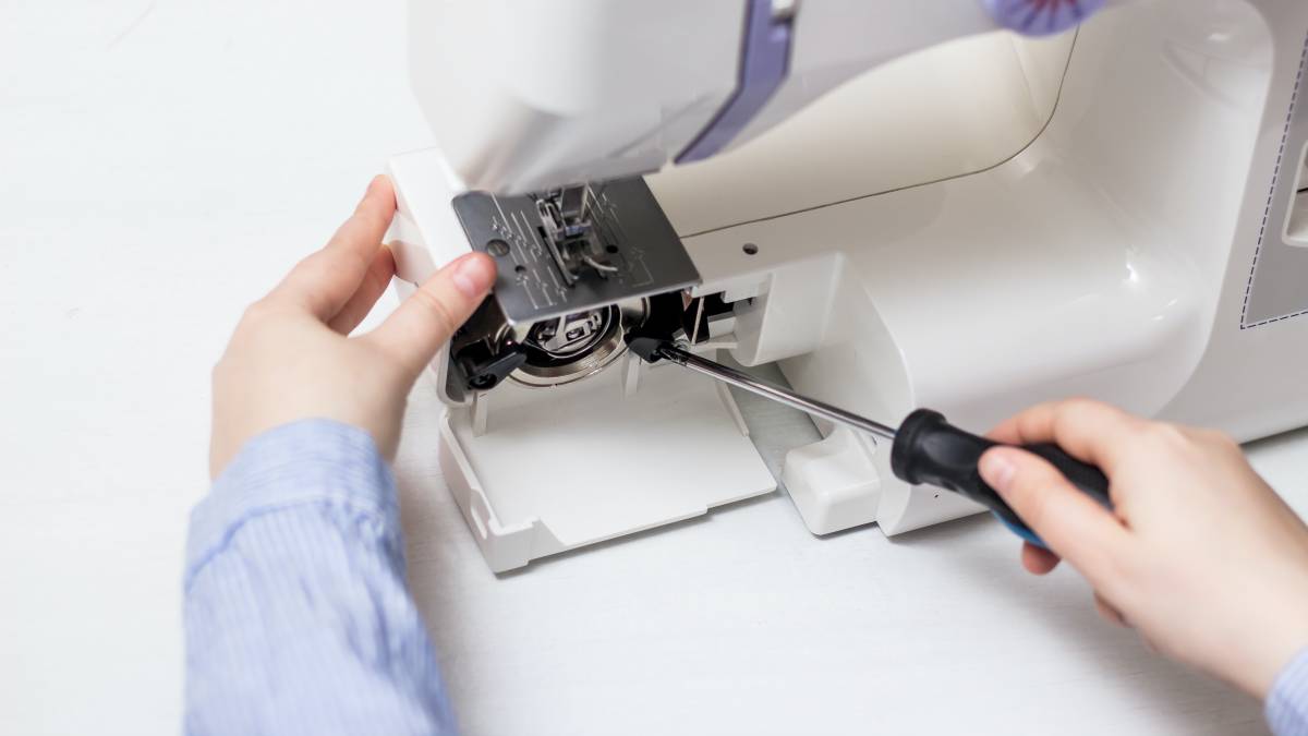 A person carefully using a screwdriver to open the bobbin area of a sewing machine for maintenance or repair. 