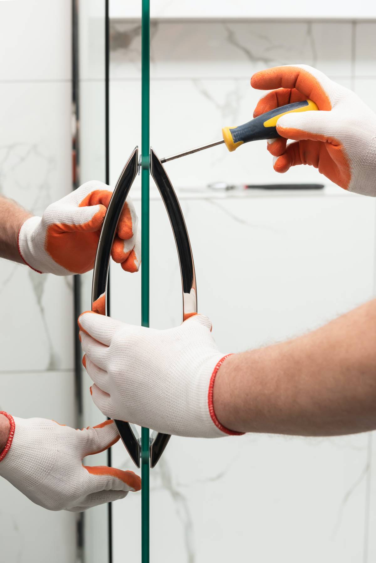 Two pairs of hands wearing orange gloves installing a glass shower screen