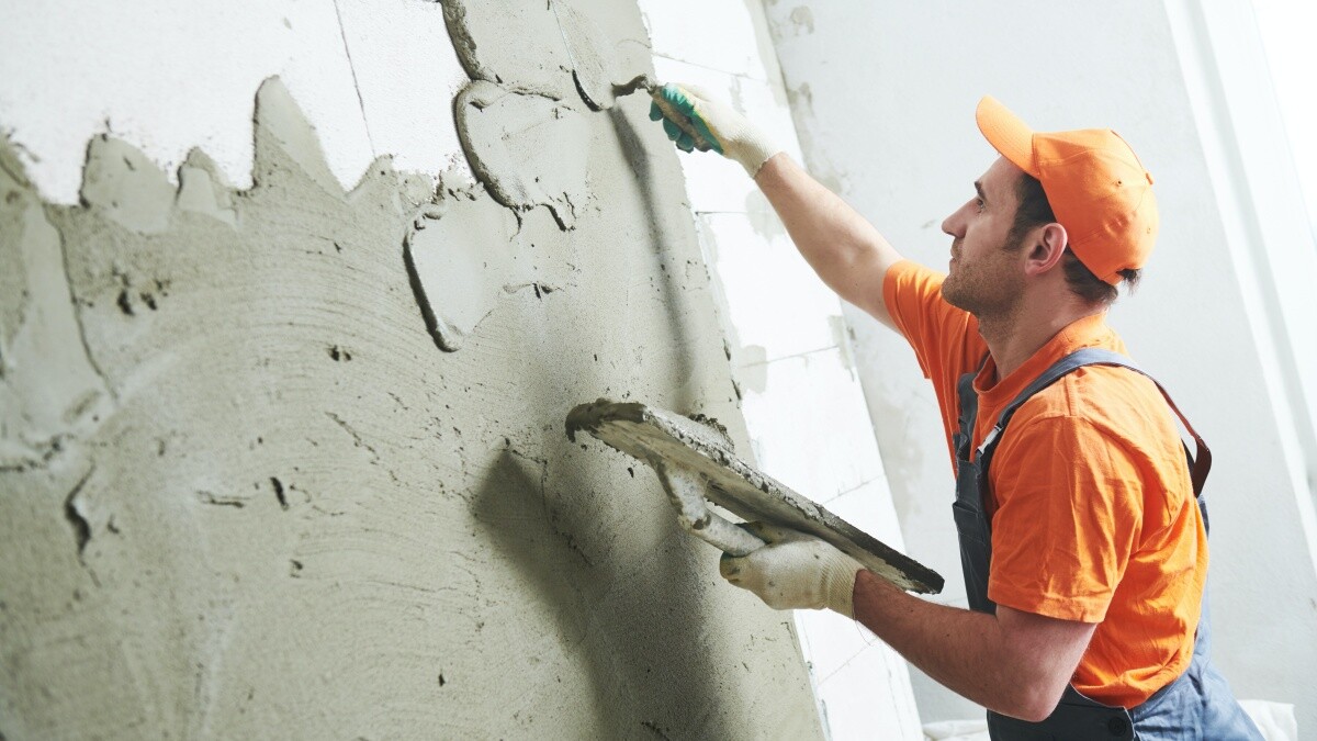 man wearing orange overalls plastering wall