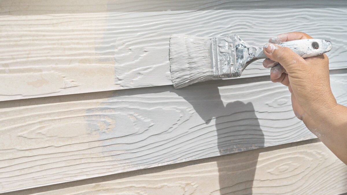 painter using white paint painting a wood wall